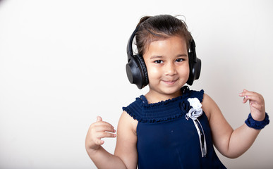 Cute little girl with headphones listening music  giving cute expression and smile on face