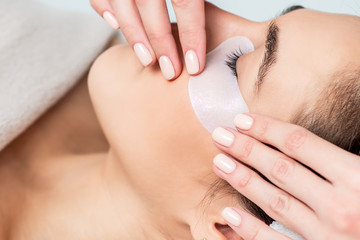 Wall Mural - Cosmetologist hand putting strip under woman eye before eyelash extension procedure.