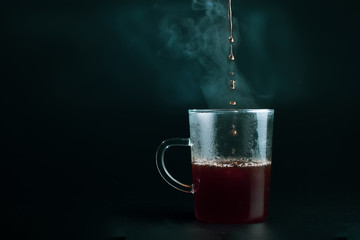 Hot black coffee, pour into a clear glass On a black background.