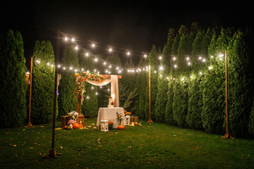 night wedding ceremony, the arch is decorated with flowers, candles and garlands of light bulbs and there is a wedding cake on the table