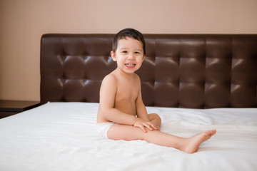 Cute toddler boy in diapers lies on bed with white sheet