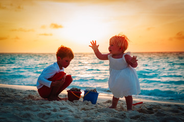 little boy and girl play with sand on beach at sunset