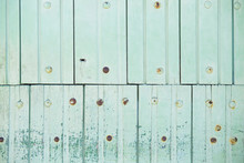 Painted Old Wooden Green Fence Made Of Boards With Rusty Nails And Peeling Paint. Light Green Background.