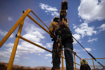 Safe workplace rigger wearing working at heights harness clipping an inertia reel shock absorbing fall arrest device hook on the rope sling anchor point while working from 2 metre exposure open edges 