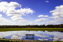 A Wooden Bench Surrounded By Flooded Water And Blue Sky With Clouds