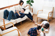 Young Asian love family stay in living room at home, two daughter playing drawing by color pencil together with fun on wooden floor, parents relaxing by reading book and use tablet on white sofa
