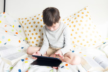 Game. Boy Plays With Smartphone. School Boy On Bed At Home With Digital Pad Tablet In Hand, Doing Homework. Distance Learning Online Education. Quarantine. Game. Boy Plays With Smartphone