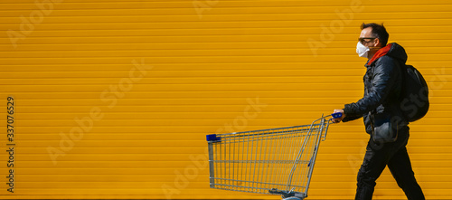 Fotografía Man with with a shopping cart in front of a store, wearing a mask during a coronavirus pandemic / Covid-19