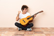 © luismolinero - Young caucasian man with a guitar sitting on the floor celebrating a victory