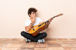 © luismolinero - Young caucasian man with a guitar sitting on the floor with surprise and shocked facial expression