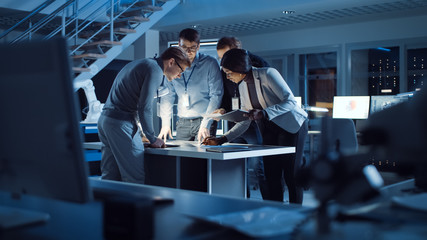 Fototapete - Diverse Team of Electronics Development Engineers Standing at the Desk Working with Documents, Solving Project Problems Late at Night. Specialists Working on Ultra Modern Industrial Design.