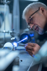 Fototapete - Portrait of Focused Middle Aged Engineer in Glasses Working with High Precision Laser Equipment, Using Lenses and Testing Optics for Accuracy Required Electronics