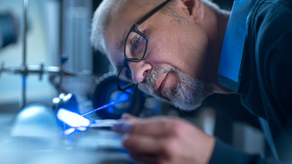 Wall Mural - Close-up Portrait of Focused Middle Aged Engineer in Glasses Working with High Precision Laser Equipment, Using Lenses and Testing Optics for Accuracy Required Electronics