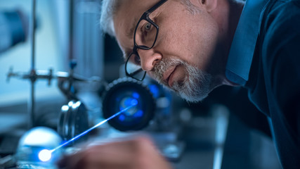 Poster - Close-up Portrait of Focused Middle Aged Engineer in Glasses Working with High Precision Laser Equipment, Using Lenses and Testing Optics for Accuracy Required Electronics