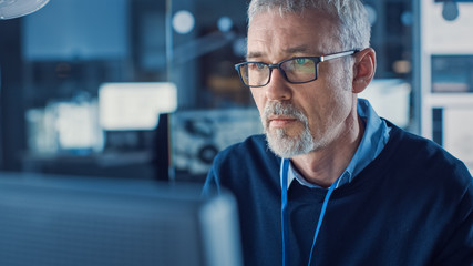 Fototapete - Portrait of Handsome Middle Aged Engineer Wearing Glasses Works on Personal Computer. In the Background High Tech Engineering Facility.