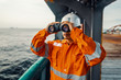 © Igor Kardasov - Filipino deck Officer on deck of vessel or ship , wearing PPE personal protective equipment. He is looking through binoculars.