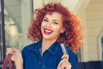 Cheerful smile woman holding showing credit card near clothing department store shopping mall outdoor Curly red head happy girl with visa at retail shop Shopaholic concept pay with credit card banking