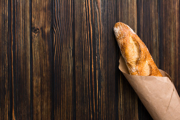 Fresh french crisp bread wrapped in craft paper. Trendy healthy food concept for banner on dark wood background, top view