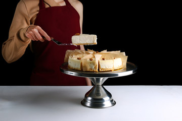 Wall Mural - cheesecake with almond. confectioner hold dessert on pastry shovel. Classic dessert cheesecake isolated on black