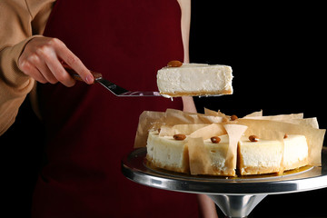 Wall Mural - cheesecake with almond. confectioner hold dessert on pastry shovel. Classic dessert cheesecake isolated on black closeup