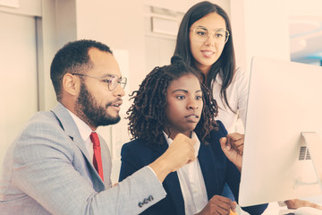 Smiling young business colleagues working with computer. Young multiethnic business people using desktop computer in modern office. Business and technology concept