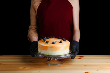 Wall Mural - orange cake with berries and rosemary closeup on table. dessert isolated on black. mousse marble cake with decorating confectioner hold cake