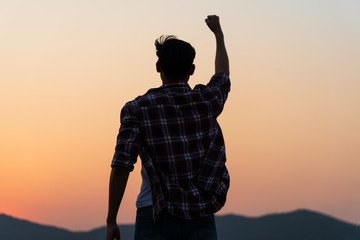 Man with fist in the air during sunset sunrise mountain in background. Stand strong. Feeling motivated, freedom, strength and courage concept.