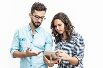 Serious puzzled couple reading message on tablet screen. Young woman in casual and man in glasses in glasses posing isolated over white background. Networking concept