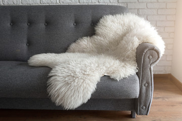 White sheep skin on a gray sofa. A cozy place to relax in the apartment