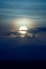 Canvas Print - Big sun in sunset sky are drowning behind the mountain.