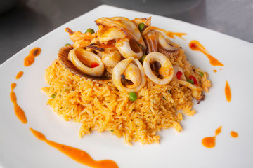 Wall Mural - Peruvian food: arroz con mariscos or rice with seafood decorated with squid and clam, served on a white plate