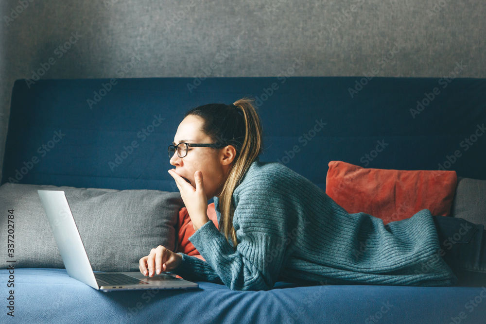Girl yawns while working at a laptop. She is tired or overworked or has insomnia. - obrazy, fototapety, plakaty 