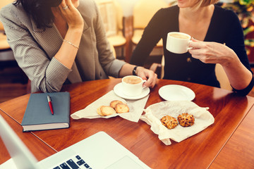 Two women colleagues drink coffee and eat cookies.