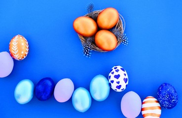 Poster - Golden Easter eggs in a nest with feathers, multi-colored Easter eggs on a blue background. Copy space