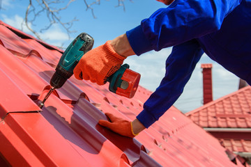 Wall Mural - Close up of young man worker in blue overall fix a metal tile roof