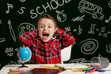 Emotional school boy sitting on the desk with many school supplies. First day of school. Kid boy from primary school. Back to school. Child from elementary school.