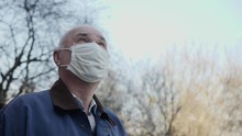 Portrait Of Elderly Man With Handmade Mask On His Face To Protect Himself From Coronavirus Pandemic. Close-up Of Man Standing Outdoors Looking Up At The Sky. Concept Of Hope, Faith, Health And Safety