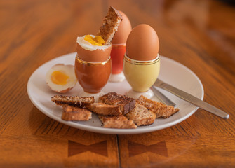 Soft boiled eggs and toast soldiers on a white plate with 60's style egg cups