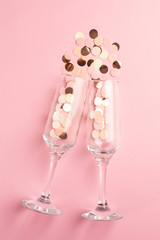 Champagne glasses with pink and gold confetti on pink color paper background minimal style