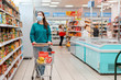 © _KUBE_ - Shopping. A young Caucasian woman with a medical mask on her face, rolls a grocery cart and selects food. Product purchase concept and virus pandemic