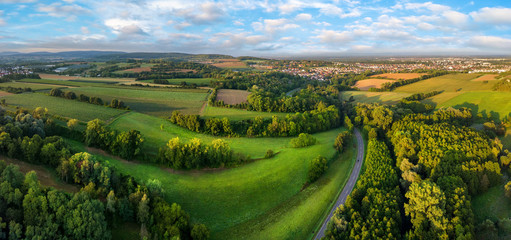 Gorgeous aerial landscape panorama after sunrise: European meadows and forests with blue sky and leading lines