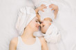 © sofiko14 - Young pretty relaxed woman mom and her cute little baby girl at home, with towels on heads after bath, lying on bed head to head, looking each other, touching noses and smiling. Happy family spa