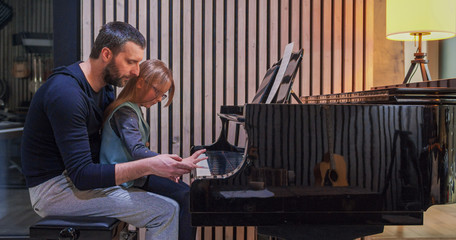 Wall Mural - Dad teaching piano to his daughter.Little girl learning piano at home.Side view.Piano class at home. Child learning piano from her father