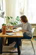 © Anastasiia Nurullina - Female artist at her workplace working from home. Woman dressed in jeans and striped shirt sitting at the table and drawing illustration.