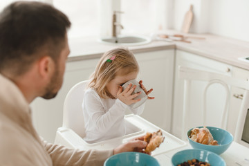 Young cute family with little daughter have breakfast at home in the kitchen.