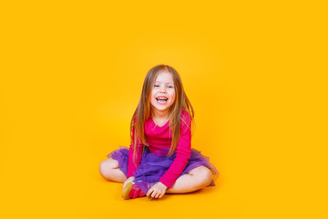 Funny cute funny fashionable little girl in pink t-shirt and purple tulle skirt sitting on yellow background