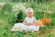 © Olga Gimaeva - a little girl 1 year old sits in the grass in light clothes, holds grapes in her hand, smiles, next to her is a basket and a bouquet of field daisies, childhood in the summer
