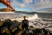 A Surfer Getting Ready To Jump In The Ocean Underneath The Golden Gate Bridge.