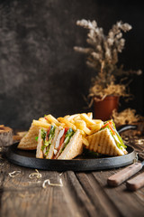 Wall Mural - Side view on sandwiches with fries on the black pan on the wooden table, vertical format