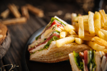 Wall Mural - Closeup on sandwiches with fries on the black pan on the wooden table, horizontal format